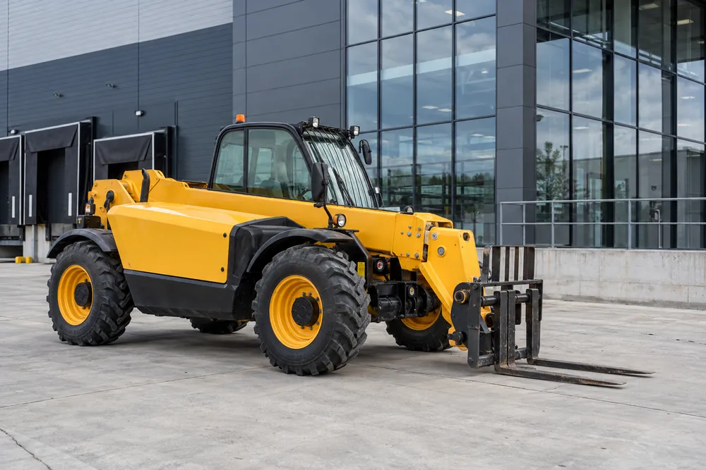 Telehandler with retracted boom and lowered forks outside a warehouse